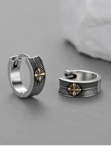 Detail shot of retro silver hoop earrings featuring feather texture and a gold cross accent.