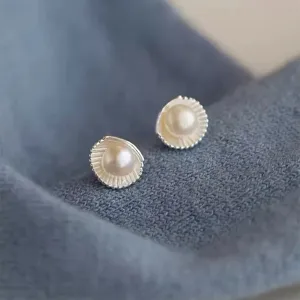 Close-up detail shot of exquisite shell pearl stud earrings with delicate metallic texture.