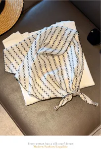 Detailed view of white triangle scarf with black chain print and beaded tie decor.