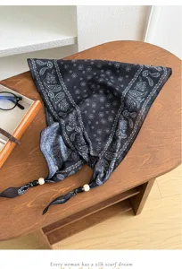 Detail shot of a black paisley printed scarf featuring pearl bead ends on a wooden desk.