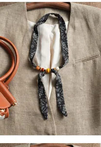 Detail view of black paisley silk ribbon neck scarf featuring colorful wooden beads closeup.