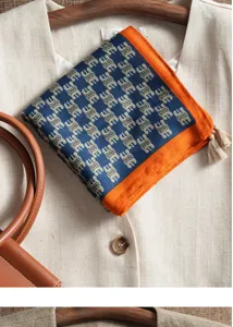 Close-up detail of the patterned silk-blend square scarf with contrast orange border and tassels.