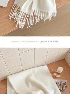 Close up detail of soft white wool scarf with fringe on wooden table cozy lifestyle.