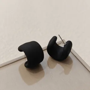 Detailaufnahme von matten schwarzen, klobigen C-formigen Creolen im minimalistischen Trend-Stil.