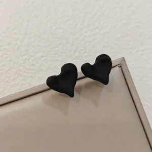 Gros plan boucles d'oreilles cœur noir mat irrégulier, design minimaliste de bijoux.