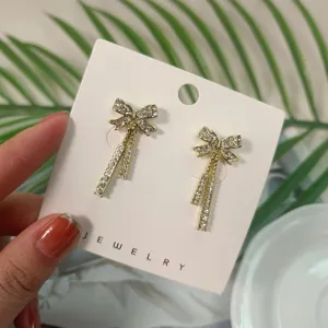 Primo piano dettagliato di eleganti orecchini pendenti con fiocco in strass dorato chiaro.