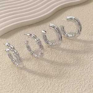 Close-up detail of silver bamboo textured hoop earrings arranged neatly on textured background.