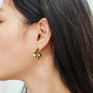 Gros plan de boucles d'oreilles créoles dorées à billes sphériques brillantes sur l'oreille.