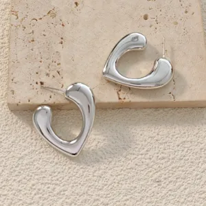 Gros plan détaillé de boucles d'oreilles créoles C cœur argentées sur fond en pierre.