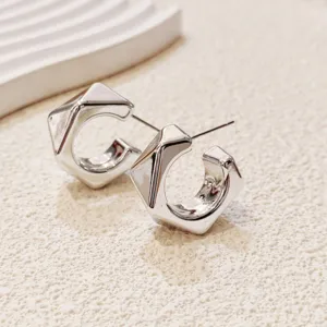 Détail de boucles d'oreilles créoles géométriques argentées, clous d'oreilles modernes.