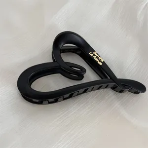 Close-up view of a matte black heart hair claw clip featuring elegant gold text details.