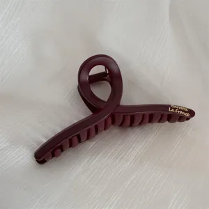 Close-up detail of the dark red matte hair claw clip featuring unique loop design and logo.