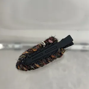 Close-up of a colorful woolen knitted hair clip, textured fabric detail on black duckbill.
