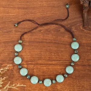 Detailed view of handmade ethnic beaded necklace with turquoise floral discs and brown cord.