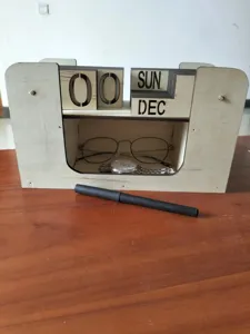Détail de calendrier perpétuel vintage en bois avec compartiment de rangement et déco de bureau.
