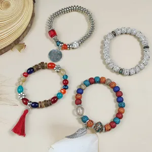 Detailed view of bohemian stackable beaded bracelets with charms and tassels on textured background.