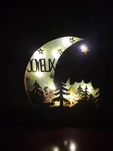 Vue détaillée de la veilleuse croissant de lune en bois avec sapins découpés et lumière chaude.