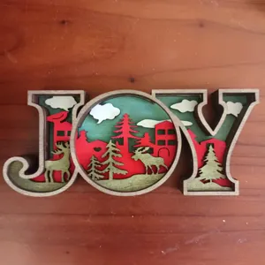 Wooden 3D Christmas JOY letter ornament with layered forest design for holiday decor.