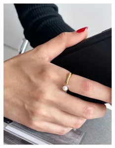 Gros plan détaillé d'une bague ouverte minimaliste avec anneau en métal lisse et perle blanche.