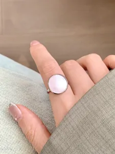 Gros plan détaillé d'une bague ronde minimaliste en coquillage rose au doigt, beau bijou.