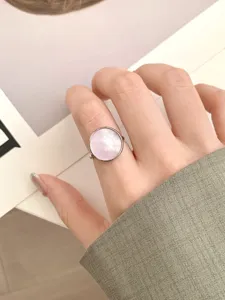 Gros plan détaillé d'une bague ronde géométrique minimaliste avec incrustation de coquillage rose.