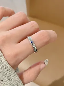 Dettaglio ravvicinato di anello geometrico in acciaio al titanio con pietra blu e zircone.