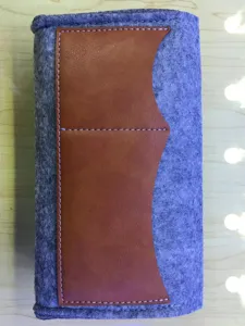 Grey felt phone pouch detail shot with brown leather pocket and white contrast stitching.