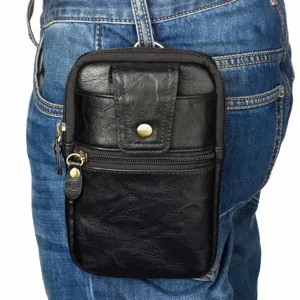Vue detaillee d etui de telephone en cuir noir accroche a la boucle de ceinture d un jean bleu.