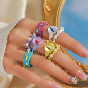 Close-up detail shot of colorful quirky eyeball resin rings with pearl accents on a hand.
