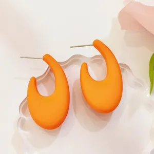 Nahaufnahme der leuchtend orangefarbenen C-förmigen Ohrstecker, minimalistischer Modeschmuck.