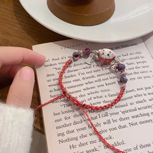 Detailed close-up of a red woven ceramic lucky cat bracelet with beads on a book page.