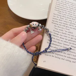 Ceramic lucky cat braided bracelet detail shot, cute woven cord with metal bell charm close-up.