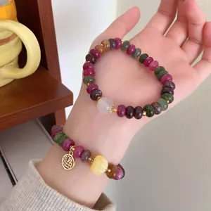 Detailed view of colorful tourmaline gemstone beaded bracelets with gold charms and carved beads.