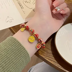 Gros plan d'un bracelet de perles émaillées cloisonnées chinoises avec des pendentifs dorés au poignet.
