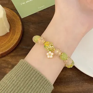 Gros plan détaillé du bracelet de perles en verre coloré avec charm fleuri porté au poignet délicat.