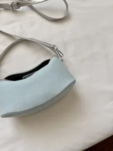 Light blue denim shoulder bag detail, stylish crescent handbag with silver strap features.