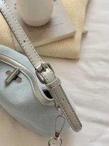 Close-up detail shot of light blue canvas shoulder bag with silver metallic buckle strap.