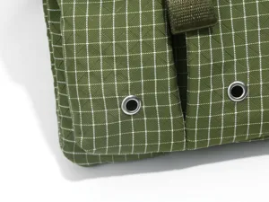Close-up of green grid workwear crossbody bag detail featuring metal eyelets and durable fabric.