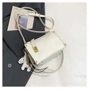 White crossbody bag detail showing metallic lock, rivets, wide strap and cute horse charm.