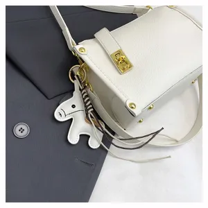 Detailed view of the white leather crossbody bag with a cute horse charm and gold-tone hardware.