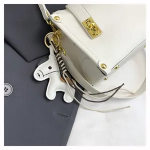 Close-up detail of white leather crossbody bag featuring cute horse charm and gold lock.
