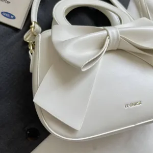 Close-up detail of white women handbag with elegant front bow and gold hardware trim.