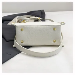 Detailed view of white leather crossbody bag bottom showing gold metal feet hardware.