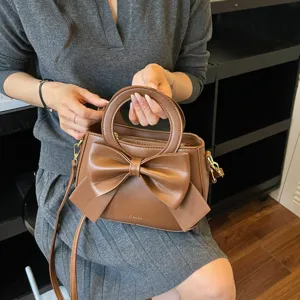 Stylish brown handbag for women with elegant front bow design, top handle and shoulder strap.