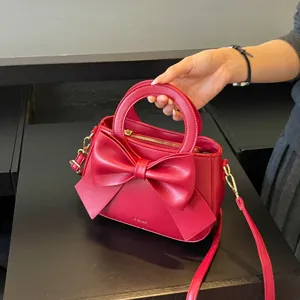 Red PU leather handbag detail view featuring a chic front bow and elegant circular handle.