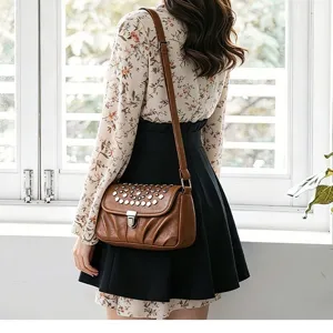 Detailed view of retro brown leather shoulder bag with metal studs and clasp, worn by model.
