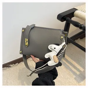 Grey leather crossbody bag detail view featuring wide shoulder strap and cute horse charm.