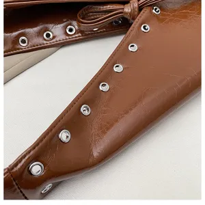 Brown patent leather bag detail showing metallic eyelets and strap design. Perfect accessory.