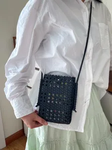 Dettaglio della borsa a tracolla intrecciata nera indossata dal modello, con motivo elegante.