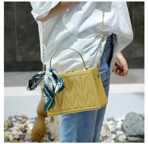 Close-up detail of a chic yellow quilted box bag with metal handle and stylish scarf.